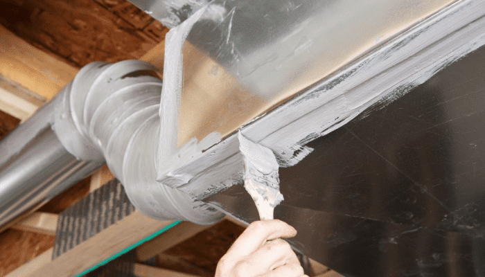 Technician applying sealant to basement ductwork to eliminate musty odors and improve air quality.